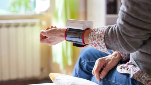 Senior patient measuring blood pressure with a wrist monitor while seated at home near a curtained window