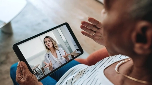 Older adult holds a tablet during a video consultation with a healthcare professional