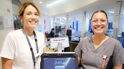 Two healthcare workers smile beside a medical interpreter tablet in a hospital