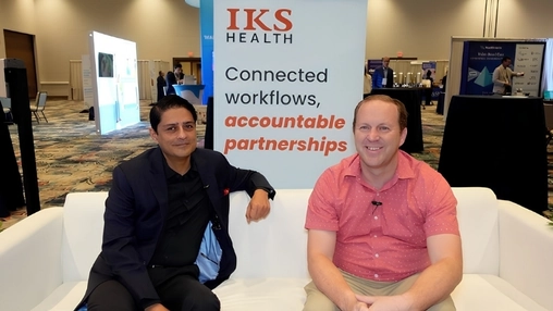 Two men on a white sofa at a healthcare conference in front of an IKS Health Connected workflows banner