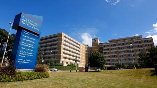 University of Mississippi Medical Center entrance sign and brick hospital complex under a clear blue sky